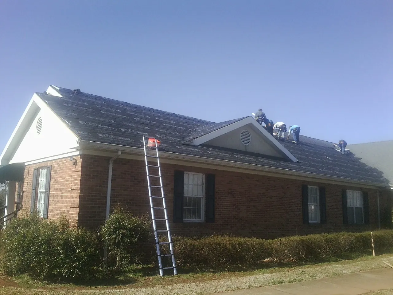 Crew tearing shingles off a brick ranch roof with a ladder set — Emergency Roof Repair work by our crew in Lehi