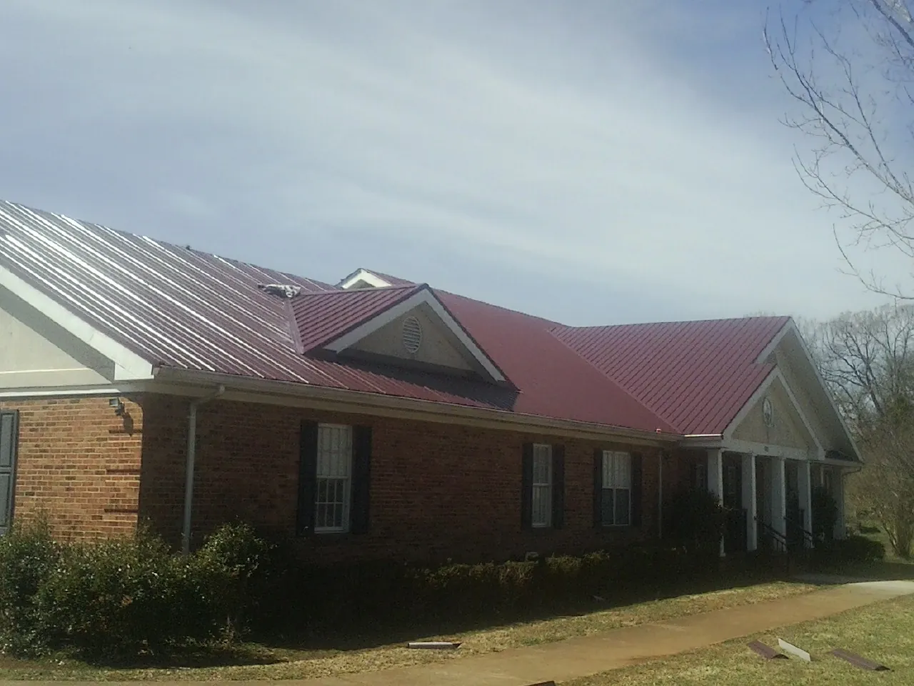 Red metal roof with gabled entries on a long brick building, from a Hail Damage Roof Repair job in Lehi
