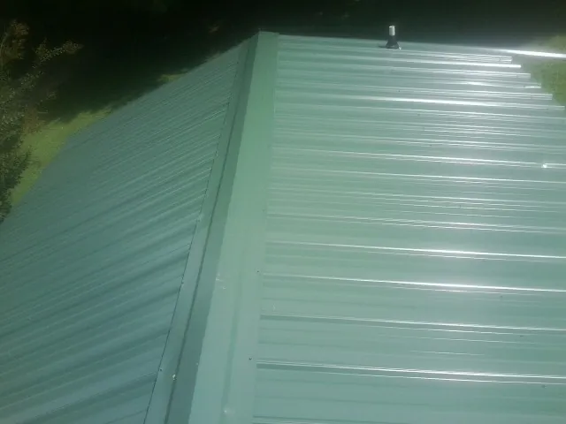 New green metal panels meeting at the ridge of a roof — Flat Roof Repair work by our crew in Lehi