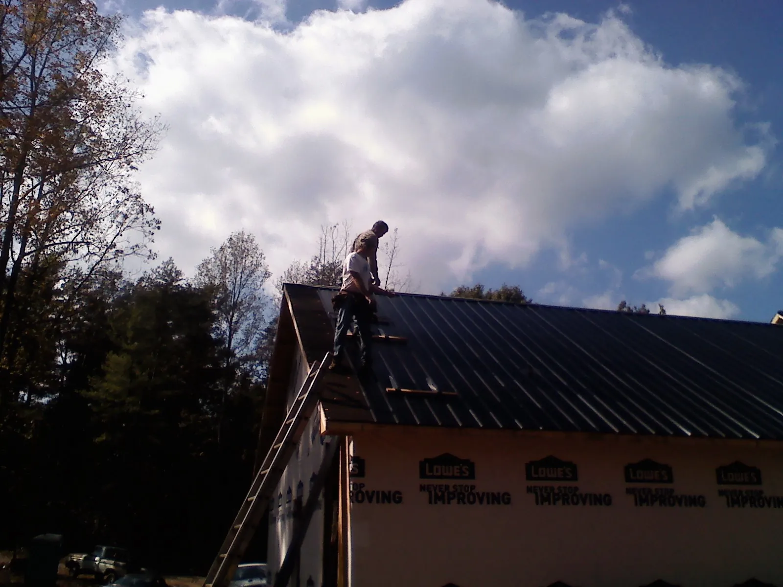 Roofer fastening dark metal panels high against a cloudy sky, from a Roof Inspection job in Lehi