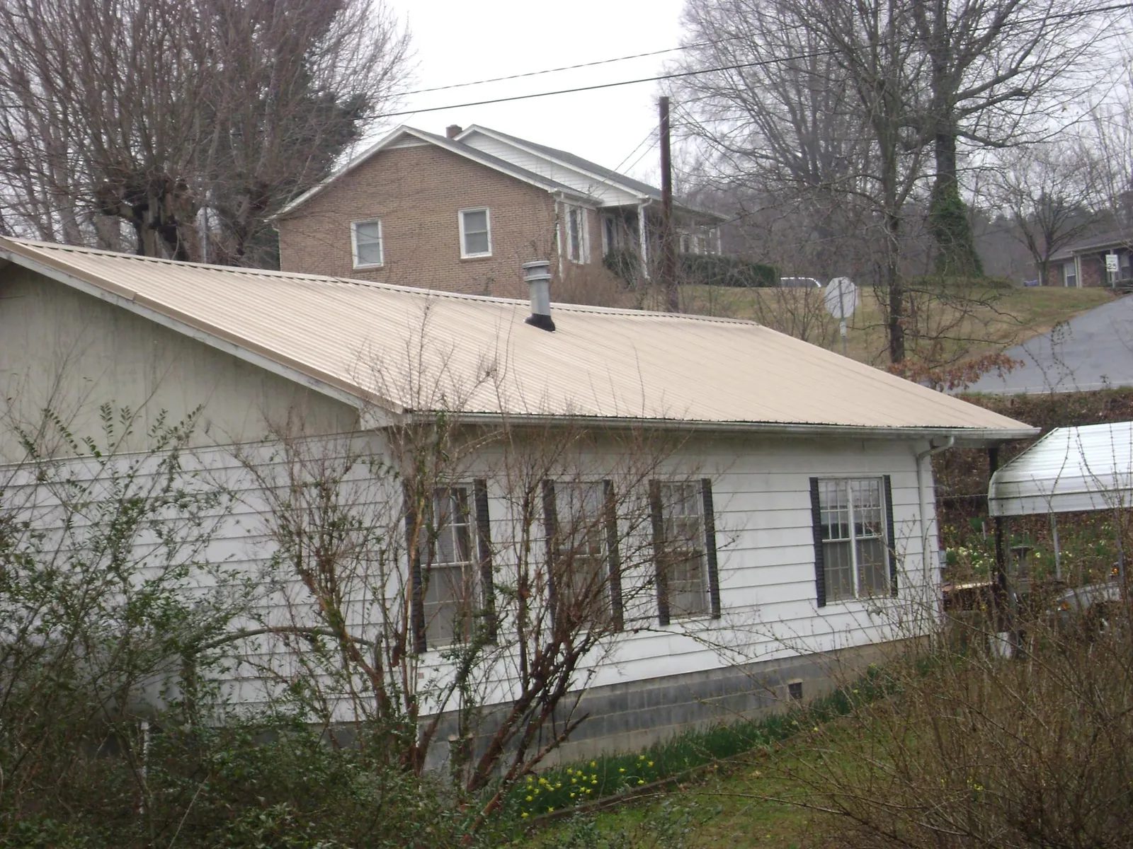 Tan metal roof on a white sided house set into a hillside — Commercial Roofing by Roofing Brothers in Lehi